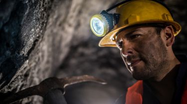 Miner working at a mine underground wearing a helmet with light and using one of his tools